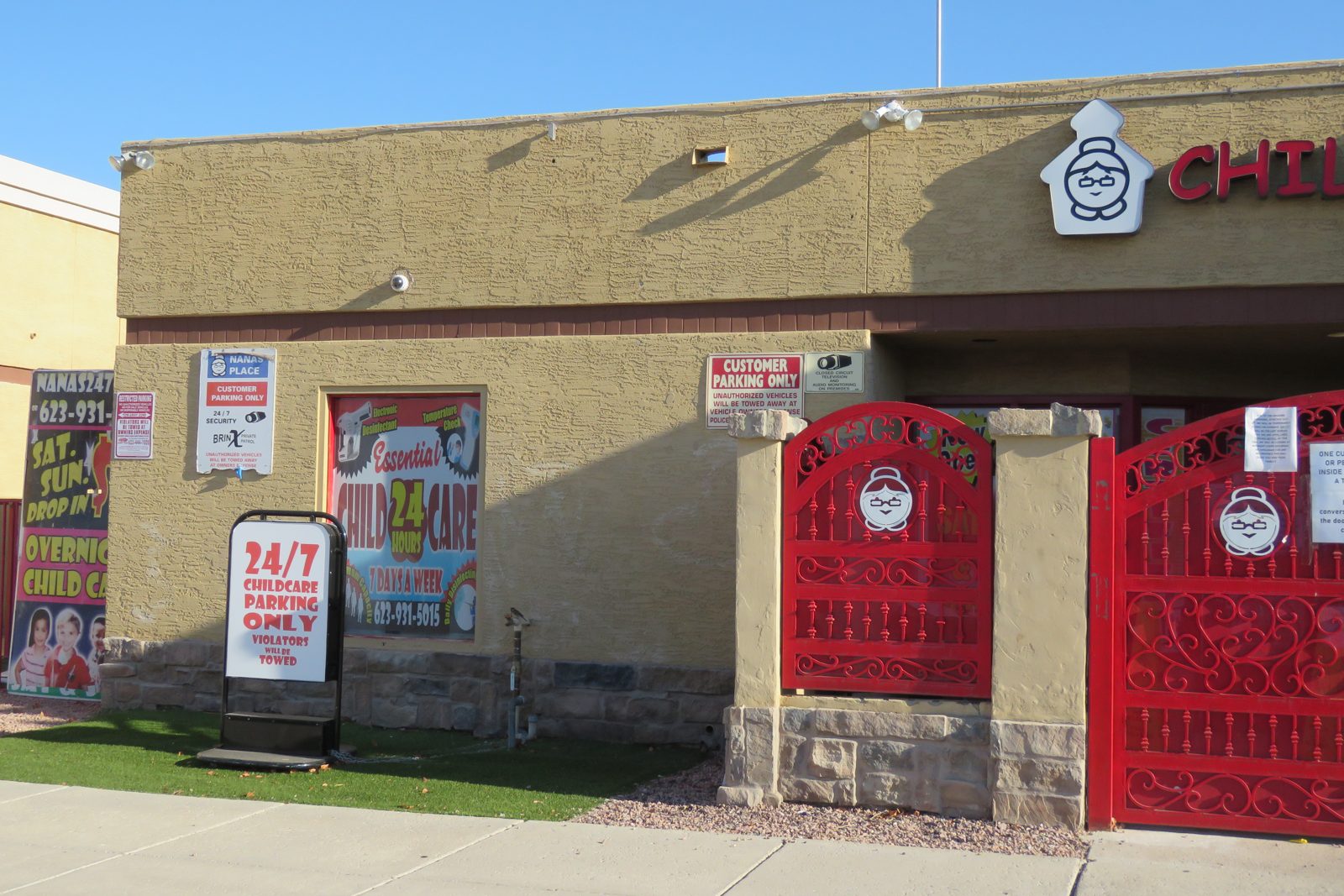 The front of Nana&rsquo;s: the grandmother logo and CHILD CARE in red letters
 above red iron gates, with signs reading 24/7 Childcare, Overnight Child Care
 and Sat. Sun. Drop In.